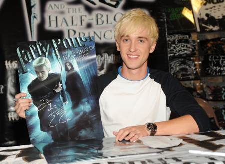 Tom Felton sonriente firmando un poster