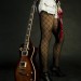 Guitarra Les Paul color café oscuro Chica que muestra sus piernas en compañía de una guitarra Les Paul