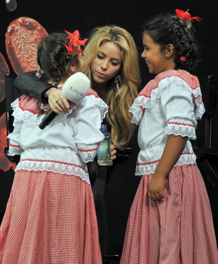 Shakira abrazando a dos niñas que visten trajes tipicos