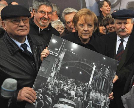 Mikhail Gorbachev y  Lech Walesa ayudan a la canciller alemana a sostener una foto de 1989 del puente Bornholmer  ayudan a la canciller alemana a sostener una foto de 1989 del puente Bornholmer