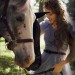 Miley Cyrus posando alado de un caballo con lindo vestido gris