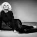 Christina Aguilera posa recostada en el suelo, vistiendo pantalones ajustados de cuero y una blusa color negro.