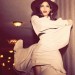 Freida Pinto posando con la falda alzada con un vestido amplio color beige de mangas largas y un sombrero café de ala ancha muy retro.